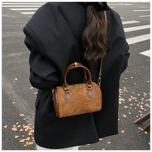 Detail einer braunen Wildleder-Bostontasche mit geprägtem Schriftzug und Riemen