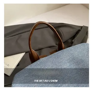Detail of blue denim fabric bag with thick brown leather handles and fine stitching