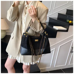 Detail of black quilted suede tote bag with chain strap and gold turn-lock on the stairs