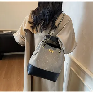Dettaglio di una borsa a secchiello trapuntata con catena indossata con un trench coat