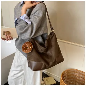Detail van de bruine suède tas met contrasterende stiksels en een donut-bedeltje eraan