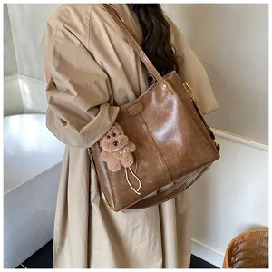 Detailopname van een bruine shopper met metalen klinknagels en een pluche beer hanger