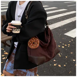 Detail van bruine suède tote bag met witte contraststiksels en pluche donut hanger