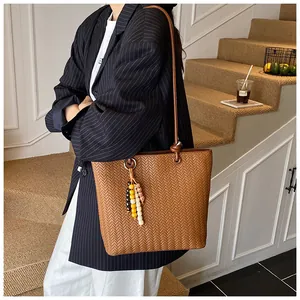 Gros plan sur un sac cabas tressé marron avec pendentif en perles et texture tissée
