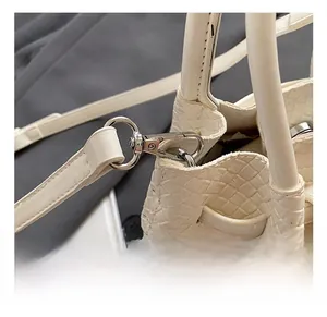Close-up of white woven bucket bag with shiny silver metal hook and detachable strap