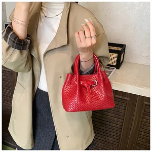 Detail of red woven handbag with Intrecciato pattern and buckle held by a model