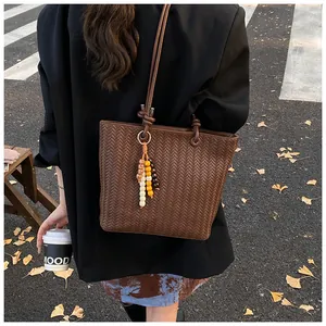 Détail du cabas tressé marron foncé avec gland en perles colorées sur fond de rue