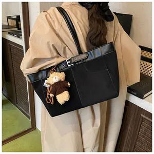 Detail of black canvas tote bag with leather trim and a cute plush bear charm accessory