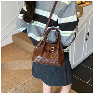 Detail view of dark brown woven bucket bag worn by model on stairs in a home setting