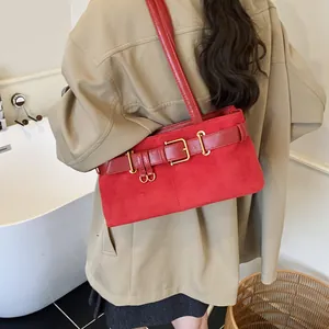 Bolso de hombro de ante rojo con hebilla dorada mostrado en una modelo con estilo