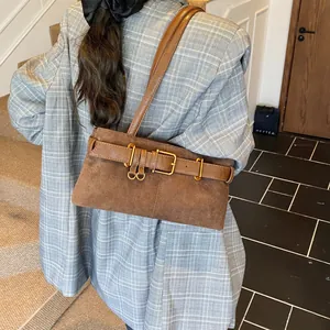 Bolso bandolera de ante marrón con hebilla dorada mostrado al hombro por el modelo