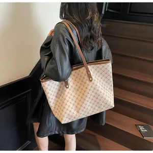Detail view of beige tote bag with brown leather handles and geometric monogram pattern