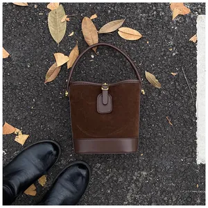 Close-up of a brown patchwork bucket bag with suede texture on a leafy asphalt road