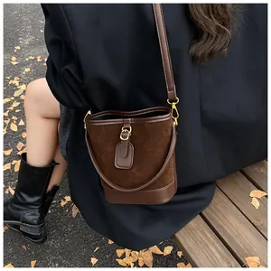 Detail of dark brown suede bucket bag with gold hardware worn against a winter coat