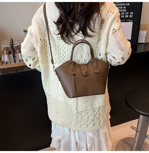 Sac seau en cuir marron grainé porté en bandoulière par un mannequin dans un café