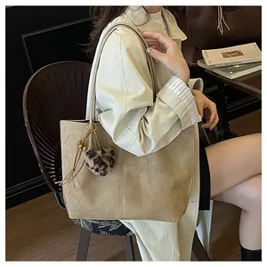 Macro shot of light brown suede tote bag with leopard print pom-pom charm on a beige coat