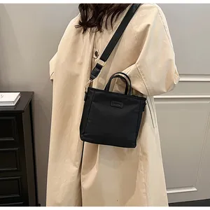 Detail view of a black nylon tote bag worn with a beige trench coat for a stylish look
