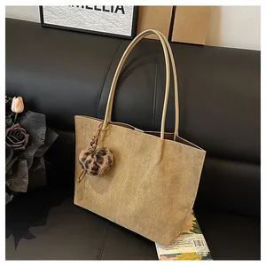 Macro view of khaki suede tote bag with leopard heart charm on a black leather sofa