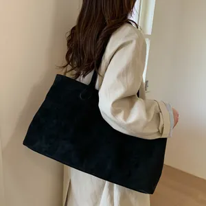 Minimalist large black suede tote bag shown on shoulder over an apricot trench coat