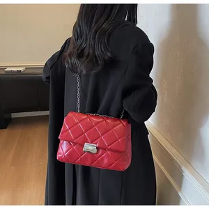 Close-up of red quilted chain bag with silver buckle worn by a model in a warm setting