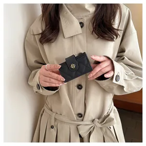 Close-up of black quilted leather card holder with gold clover clasp held by hand