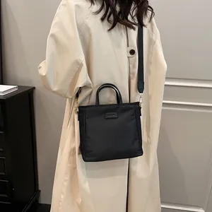Minimalist black nylon tote bag with wide adjustable strap and brand logo detail