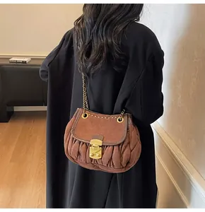 Détail d'un sac selle en daim marron avec chaîne dorée et broderie plissée