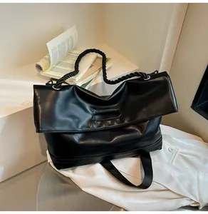 Detail of large black tote bag featuring woven rope straps and glossy faux leather texture