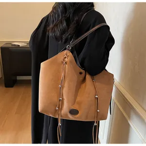 Close-up of brown suede tote bag featuring long tassels and metallic bead details