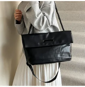 Detail of black leather tote bag featuring a hollow handle and decorative rope shoulder strap