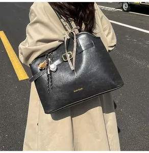 Detail of black leather tote bag featuring belt buckle and decorative baseball charm