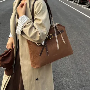 Brown suede tote bag with belt detail and plaid ribbon shown in an outdoor fashion setting