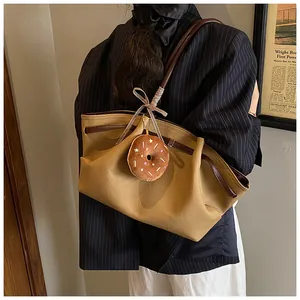 Detail view of khaki canvas tote with brown leather handles and plush donut charm