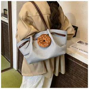 Detail of grey textured tote bag with dark brown straps and doughnut plush charm