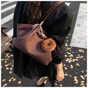 Detail of dark brown wool tote bag featuring leather handles and donut plush charm