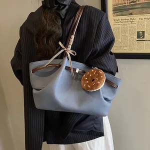 Large blue canvas tote bag with brown leather straps and a donut charm for daily commute