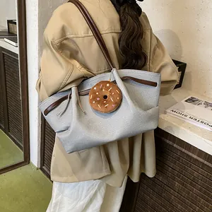Grey canvas tote bag with brown straps and cute donut pendant worn over the shoulder