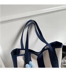 Detail of striped canvas tote bag with LEBATELEUR patch and blue ribbon charm