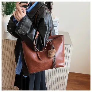 Dettaglio della borsa tote vintage in pelle marrone con logo e ciondolo a orsetto