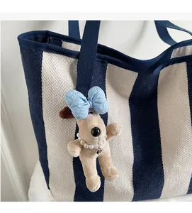 Close-up of a plush dog charm with a blue bow and pearl necklace on a striped tote bag