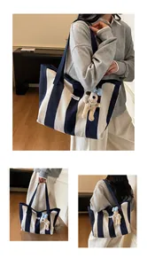 Detail of striped canvas tote bag featuring dog plush charm and logo woven label