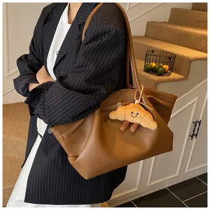 Brown lychee leather tote bag with a croissant plush charm worn by a model