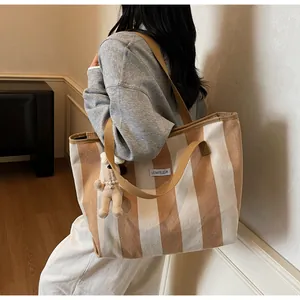 Detail of striped canvas tote bag with LE BATELEUR label and plush bear charm