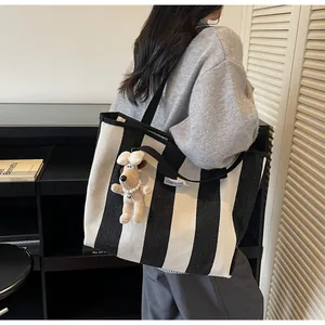 Detail of striped canvas tote bag featuring a plush puppy charm and brand label