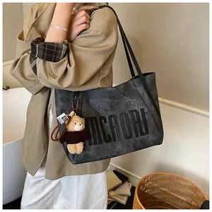 Detailed view of grey tote bag with MCAORI lettering and teddy bear charm on shoulder