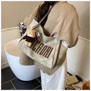 Detail of grey-beige tote bag featuring KILADAQI lettering and a cute bear charm