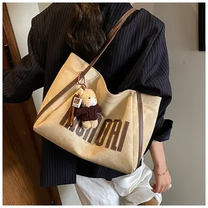 Close-up of a large beige tote bag with brown leather letters and a cute bear charm