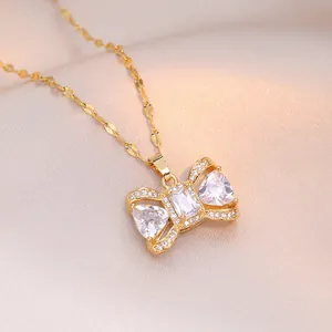 Ketting met zirkonia strikhanger in goudkleur op champagne zijden stof achtergrond