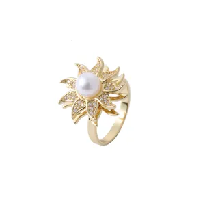 Anello a fiore dorato con perla bianca e petali di zirconi lucidi su sfondo bianco