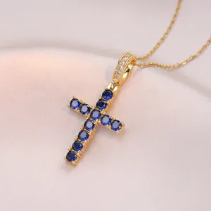 Collana con ciondolo a croce dorata con zirconi blu scuro su sfondo di seta rosa cipria